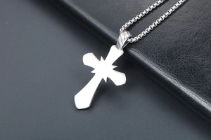 Détail d'un pendentif croix en acier titane avec motif étoilé sur une chaîne maille vénitienne