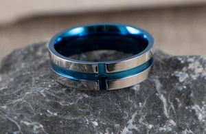 Macro detail of silver stainless steel ring with blue inner band and cross engraving