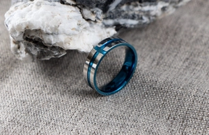 Close-up of blue and silver stainless steel ring with brushed texture and cross detail
