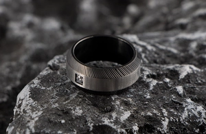 Close-up of matte black stainless steel men's ring with a single diamond and brushed texture