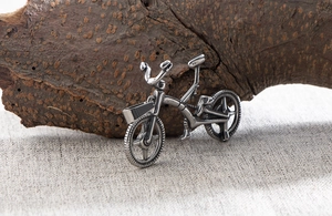 Macro detail of vintage silver bicycle pendant showing spokes and handlebar textures