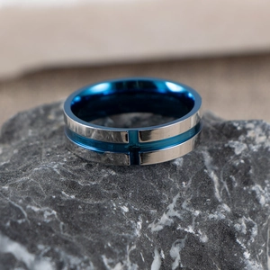 Blue and silver stainless steel cross ring for men on a dark rock background