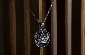 Détail macro du pendentif Œil de la Providence en acier titane sur chaîne sur fond de bois