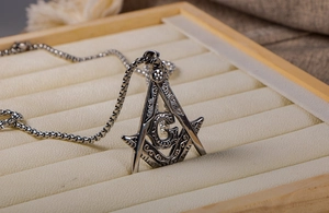 Macro view of vintage silver Masonic square and compass pendant on thick box chain