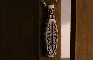 Macro shot of gothic steel coffin pendant with skull detail and cross engraving on wood