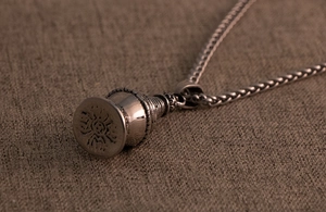 Macro detail of retro pagoda pendant with lotus base and woven metal chain on burlap