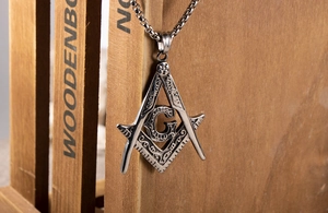 Close-up of silver steel Masonic compass pendant with letter G on a wooden board