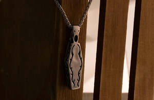 Gothic coffin pendant necklace with intricate carvings hanging on a dark wood background