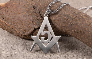 Close-up of Masonic compass and G letter pendant on textured bark with box chain