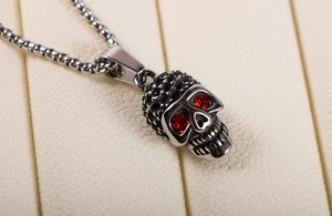 Macro detail of gothic skull pendant with red rhinestone eyes on a steel box chain
