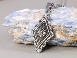 Dettaglio macro del ciondolo a rombo argento con incisione a raggiera vintage su pietra blu
