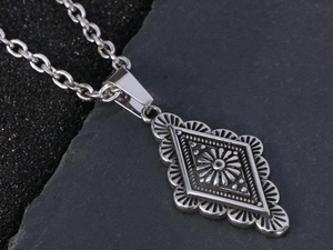 Dettaglio della collana con ciondolo a rombo vintage e motivo a sole su sfondo di pietra