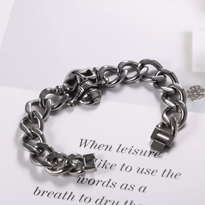 Detail of gun black punk cuban chain bracelet with a carved skull charm on display card