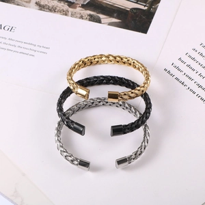 Three-color twisted metal cable open bracelets in gold, black, and silver on stone