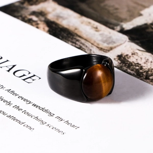 Men's black stainless steel ring featuring a round tiger eye stone on a magazine background