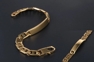 Detailed macro view of gold anchor link bracelet with polished metal ID plate and clasp