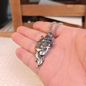 Detailed view of an antique silver mask pendant featuring ethnic embossed carvings and patterns