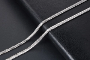 Detailed close-up of a silver snake chain necklace on a premium black leather background