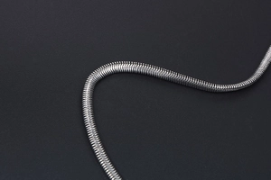 Macro shot of a sleek silver snake bone chain necklace with metallic luster on grey background