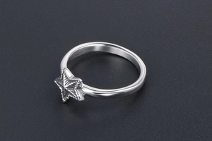 Gros plan d'une bague en acier poli avec un motif d'étoile en 3D sur fond gris mat