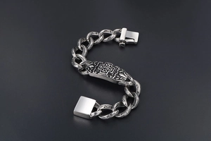 Macro detail of gothic cross plaque on thick stainless steel curb chain bracelet