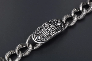Macro shot of punk style steel chain bracelet with embossed cross on a silver plaque