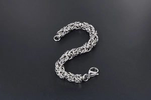 Detailed macro view of silver Byzantine weave steel chain bracelet with lobster clasp