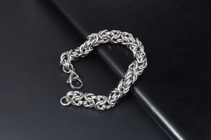 Macro shot of silver Byzantine chain bracelet with lobster clasp on leather background