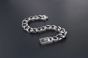 Macro view of detailed floral carvings on the rectangular clasp of a silver steel Cuban chain