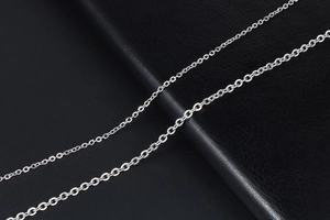 Close-up of polished titanium steel O-link chains in two different sizes on leather surface