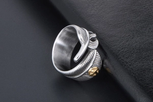 Close-up of vintage silver feather ring with gold emblem on black leather texture