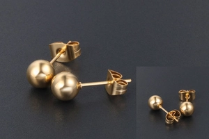 Gros plan sur des boucles d'oreilles boules dorées en acier titane avec fermoirs papillon