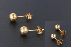 Gros plan sur les boucles d'oreilles boules dorées minimalistes avec finition miroir et fermoir papillon