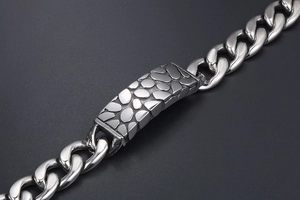Macro shot of silver titanium steel pebble texture charm on chunky curb chain bracelet