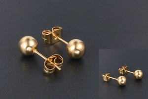 Gros plan de boucles d'oreilles boules dorées polies avec fermoirs papillon sur fond sombre