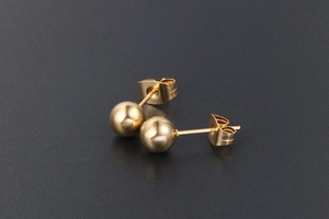 Gros plan de boucles d'oreilles boules dorées polies sur fond sombre texturé