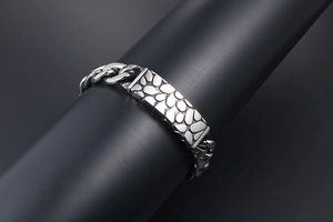 Macro detail of silver titanium steel curb chain bracelet with pebble texture plate