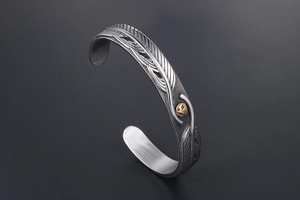 Detail of vintage eagle feather bangle with gold relief on oxidized titanium steel