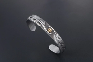 Macro view of vintage titanium steel cuff with feather texture and gold eagle stud