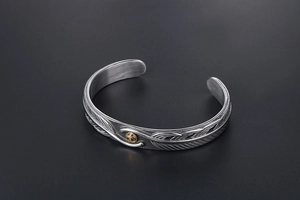Detailed macro shot of vintage titanium steel cuff with feather texture and golden eagle seal