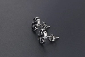Detail of cross pattée stud earrings with black enamel finish on matte background