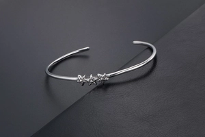 Détail du bracelet jonc en acier argenté avec étoiles sur un fond sombre texturé