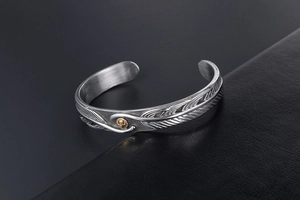 Detailed close-up of retro silver feather bangle with a gold emblem and brushed metal texture