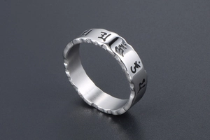 Close-up of vintage steel ring with engraved black Sanskrit symbols and grooved edges