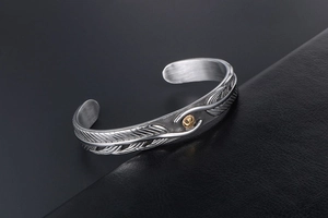 Macro shot of vintage titanium steel cuff featuring feather carvings and a gold emblem