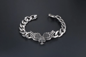 Macro detail of punk skull and wings motif on stainless steel cuban chain bracelet