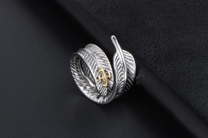 Détail macro d'une bague plume vintage montrant la texture argentée et l'emblème de croix