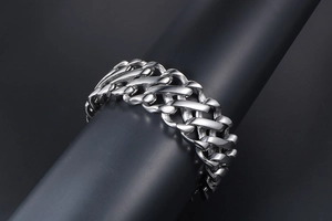 Detailed close-up of a wide silver stainless steel punk Cuban chain bracelet on a black stand