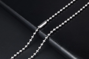 Macro shot of silver titanium steel bead chain with a smooth cylindrical clasp on leather