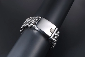 Macro shot of silver Cuban link bracelet with large rectangular clasp on black pedestal